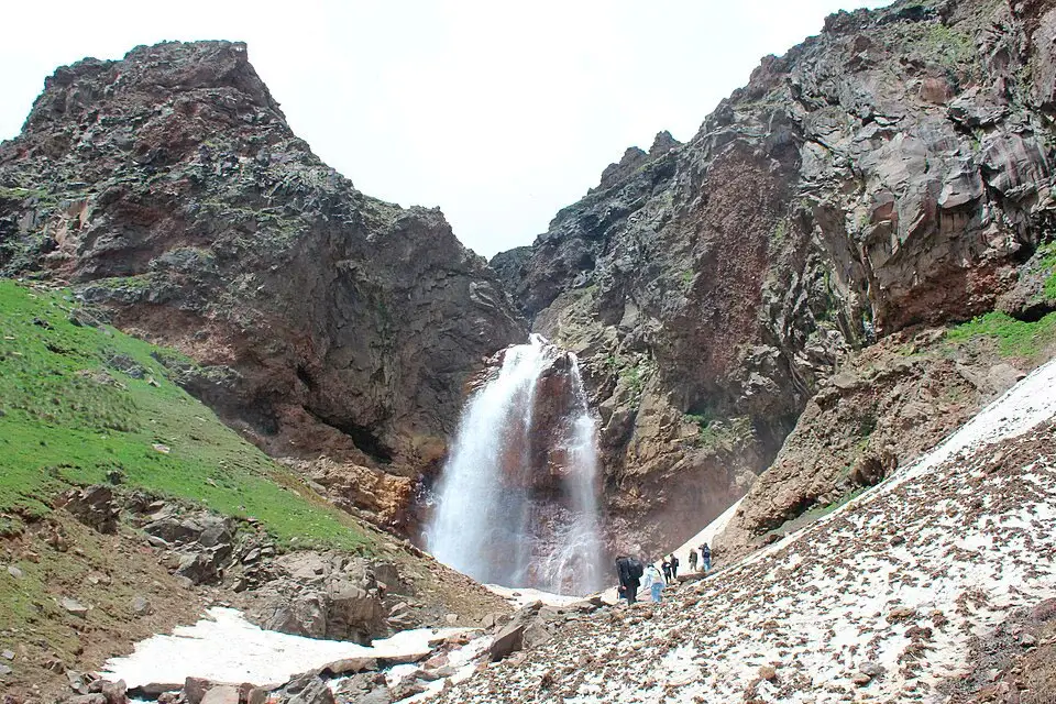 Hikers near Gegharot Waterfall among snow patches on Mount Aragats